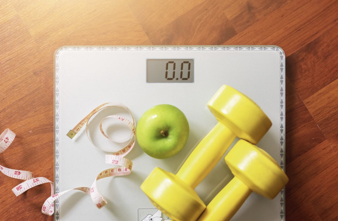 Scale, tape measure, apple, and dumbbells representing a medically supervised weight loss program